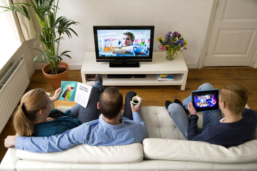 Familie op de bank met allerlei devices zoals tv, ipad en smartphone